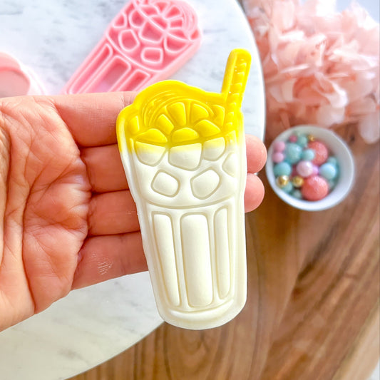 Hand holding a yellow and white ice cream mold with a straw against a blurred background.